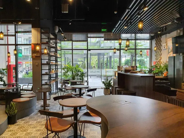 Không gian bên trong Ba Soong Coffee với bàn gỗ, đèn vàng và cửa kính nhìn ra Vinhomes Smart City